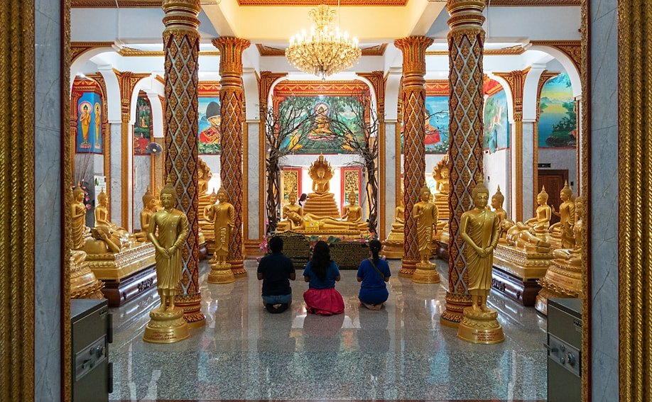 Betende Thailänder im Chedi des Wat Chalong mit goldenen Buddha-Figuren und Wandmalereien.